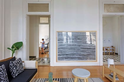 La vista hacia el pasillo paralelo al living-comedor muestra a rocío en su escritorio. Obra enmarcada de Rosario Foglia. El piso de pino tea fue recuperado e hidrolaqueado. Mesitas-banco redondas y mueble bajo (Paraná Muebles).