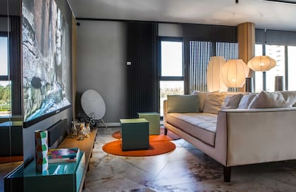 Piso de porcelanatos 'Sur Beige' de gran formato y 'Mirror Glow' (San Lorenzo Design). Sofá Lucía (Poltron Design) con géneros de Zanav. Para moderar la luz cerca de la pantalla, parasol corredizo 'Mutsharabi', un lanzamiento 2026 de Shawer.