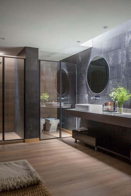 El piso ‘Fusion Vinilum’ (Patagonia Flooring) es el mismo en toda la suite. Revestimiento de pared de porcelanato (Ilva). Mesada de Silestone, bacha de apoyo y grifería (FV). Cerraron los sectores de baño y ducha con mamparas de vidrio con marco negro (Ideal Mamparas).