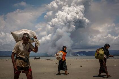 Una columna de humo se levanta en la frontera de Myanmar cuando los refugiados rohingya caminan por la orilla después de cruzar la frontera entre Bangladesh y Myanmar (11 de septiembre de 2017)