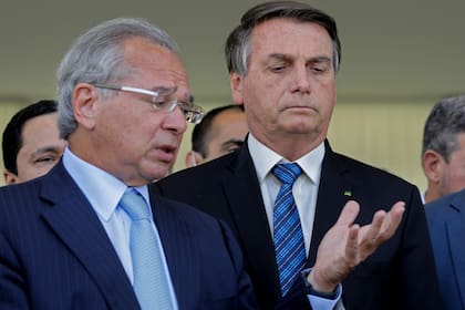 El presidente brasileño, Jair Bolsonaro (d), y el ministro de Economía brasileño, Paulo Guedes (izq.), hablan sobre ayuda financiera para brasileños vulnerables en el Palacio Planalto, en Brasilia