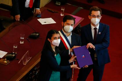 El presidente chileno Gabriel Boric, en el centro, sostiene el borrador final de la nueva constitución del país junto con los miembros de la Convención Constituyente, María Elisa Quinteros y Gaspar Domínguez, en Santiago, Chile, el lunes 4 de julio de 2022. (AP Foto/Luis Hidalgo)