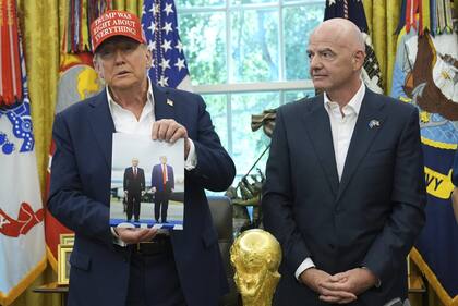 El presidente Donald Trump sostiene una foto suya junto al presidente ruso, Vladimir Putin, mientras el presidente de la FIFA, Gianni Infantino, observa durante un anuncio en el Salón Oval de la Casa Blanca.