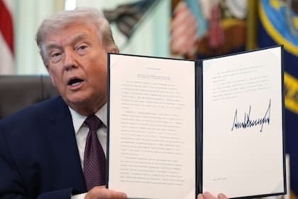El presidente Donald Trump sostiene una orden ejecutiva recién firmada en el Salón Oval de la Casa Blanca.