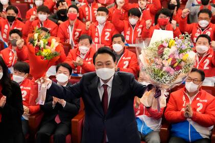 El presidente electo de Corea del Sur, Yoon Suk Yeol, sostiene ramos de flores mientras es felicitado por legisladores y miembros de su partido en la Asamblea Nacional, el 10 de marzo de 2022, en Seúl, Corea del Sur. 