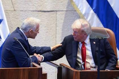El presidente estadounidense Donald Trump estrecha la mano del líder de la oposición israelí Yair Lapid en el parlamento israelí, la Knéset, en Jerusalén el 13 de octubre de 2025. Israel recibía una visita relámpago antes de una cumbre en Egipto sobre Gaza, después de que los últimos 20 rehenes israelíes supervivientes regresaran a casa tras dos años de cautiverio. La fase inicial del acuerdo de alto el fuego incluye la liberación de 47 rehenes israelíes, vivos y muertos, tomados el 7 de octubre de 2023 a cambio de 250 prisioneros y 1.700 gazatíes retenidos por Israel desde el estallido de la guerra. (Foto de Evelyn Hockstein / POOL / AFP)
