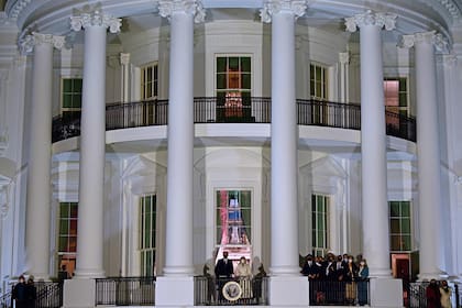 El presidente estadounidense Joe Biden (CL) y la primera dama Jill Biden (CR) aparecen en el balcón de la habitación azul mientras ellos y sus familiares (derecha) ven los fuegos artificiales desde la Casa Blanca en Washington
