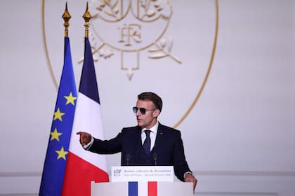 El presidente francés Emmanuel Macron, con gafas de sol, pronuncia un discurso durante la ceremonia en la que se otorgó la distinción de Caballero de la Orden Nacional del Mérito a Ali Akbar, quien vende diarios en las calles de Saint-Germain-des-Prés, en la capital francesa, desde hace 50 años