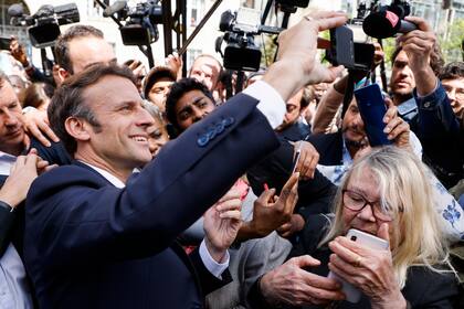 El presidente francés y candidato Emmanuel Macron se toma una selfie con residentes durante una escala de campaña el jueves 21 de abril de 2022 en Saint-Denis, en las afueras de París. (Ludovic Marin, Pool vía AP)