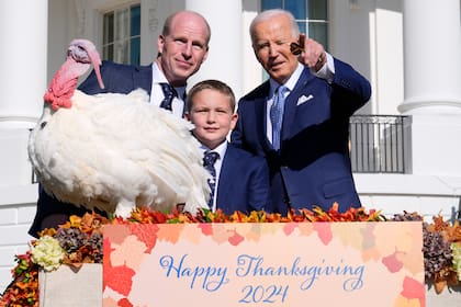 El presidente Joe Biden, derecha, señala a lo lejos junto a John Zimmerman, izquierda, presidente de la Federación Nacional de Pavos; su hijo Grant Zimmerman, al centro, y el pavo nacional del Día de Acción de Gracias, de nombre Peach, durante una ceremonia de indulto en la Casa Blanca, el lunes 25 de noviembre de 2024, en Washington. (AP Foto/Susan Walsh)