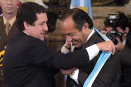 El entonces presidente provisional del Senado, Ramón Puerta, le coloca la banda presidencial a Adolfo Rodríguez Saá