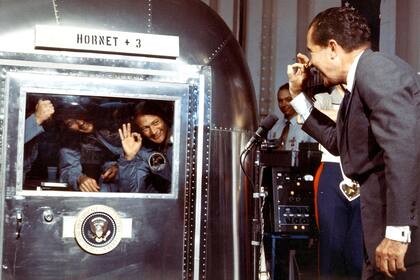 El presidente Richard Nixon saluda a los astronautas Neil A. Armstrong, Michael Collins y Edwin E. Aldrin, que se encuentran en la unidad de cuarentena luego de aterrizar de su viaje a la Luna, el 24 de julio de 1969