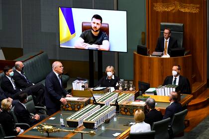El primer ministro de Australia, Scott Morrison, de pie, da la bienvenida al presidente ucraniano Volodymyr Zelenskyy en su discurso a la Cámara de Representantes a través de una videoconferencia, el jueves 31 de marzo de 2022, en Canberra, Australia. (Lukas Coch/AAP Image via AP)