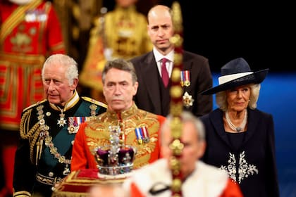 El Príncipe Carlos de Inglaterra, Príncipe de Gales (izq.), la Corona Imperial de Estado (c.), Camila, Duquesa de Cornualles (dcha.) y el Príncipe Guillermo, Duque de Cambridge (detrás c.) pasan por la Galería Real durante la Apertura de Estado del Parlamento en las Casas del Parlamento, en Londres, el 10 de mayo de 2022. 