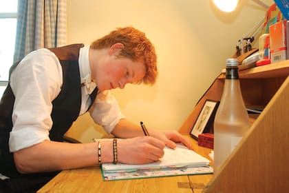 El príncipe Harry escribe en el escritorio de su habitación de Eton College, decorado con un portarretrato de su madre, Lady Di, en junio de 2003.