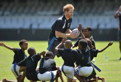 El príncipe Harry, su cuñado y antecesor en el cargo, en un partido de rugby con chicos durante una visita a Sudáfrica en diciembre de 2015.
