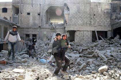 Un hombre ayuda a un chico herido en Hamouriyeh, un barrio de Ghouta Oriental