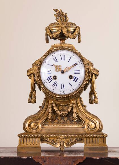 El reloj de chimenea francés, estilo Luis XVI, está decorado con guirnaldas de hojas de roble y máscaras de leones   