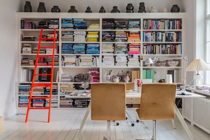 El respaldo del sillón 'Oxford' (Fritz Hansen) de la izquierda, con la famosa marca. Escalera de la diseñadora danesa Cecilie Manz. Sobre la biblioteca, urnas del estudio de Becker, r7b. En los estantes, porcelanas rosadas, herencia de su padre.