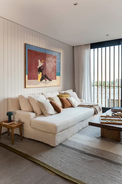 El revestimiento de machimbre está pintado en el tono ‘Domingo Nublado’ de Alba. Sillón a medida tapizado en lino y mesa ratona ‘Solid’ (Coin Vert) y pintura del artista francés Rémy De Haenen.