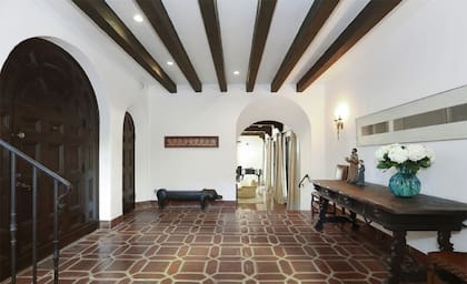 El salón de entrada, con vigas decorativas, paredes blancas y pisos de baldosas al mejor estilo colonial (Redfin)