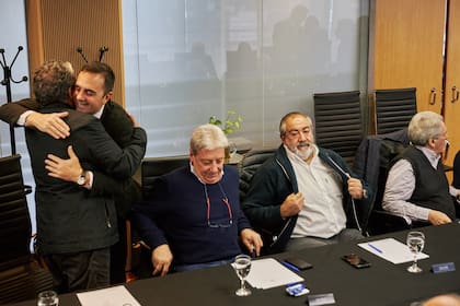 El secretario de Trabajo, Julio Cordero, se abraza a Gerardo Martínez (Uocra) en un encuentro con la CGT; observan sentados, Abel Furlán (UOM), Héctor Daer (Sanidad) y Carlos Acuña (Estaciones de Servicios)
