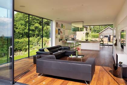 El sofá ‘Nicoletti’ de Mac and Mac Interiors y el sillón de BoConcept ceden protagonismo a la vista. Atrás, la isla de cocina separa el living del comedor, dejando las áreas sociales junto a las ventanas.