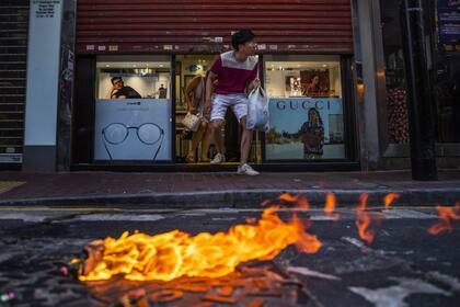 Varios clientes salen de un óptica mientras una molotov se prende fuego en medio de la calle