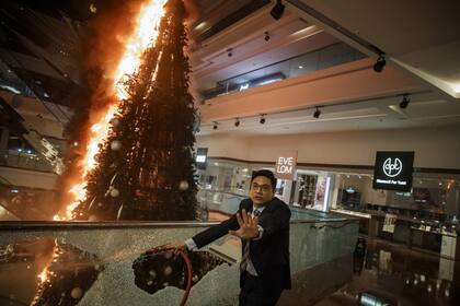 Un hombre de seguridad de un centro comercial del Festival Walk en Kowloon Tong, Hong Kong, pide precaución mientras intenta apagar un árbol de Navidad en llamas
