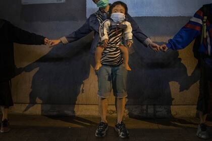 Un hombre carga a un niño mientras forma una cadena humana de solidaridad en Kowloon Bay, Hong Kong