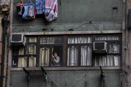 Una mujer mira por la ventana de su departamento mientras miles de manifestantes marchan por las calles de Hong Kong