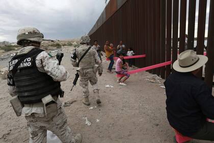 Miembros del Ejército Mexicano controlan a las personas que juegan el subibaja instalado entre la valla fronteriza que separa a México de los Estados Unidos en Ciudad Juárez