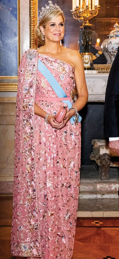 El vestido, creación de Jan Taminiau, está elaborado en jacquard con flores de distintos colores bordadas y escote asimétrico del que cae a modo de capa. Máxima de Holanda llevó, además, la banda azul de la
Orden de los Serafines.