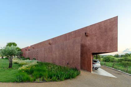 El volumen principal pigmentado con matices terrosos ofrece un frente ciego hacia la entrada vehicular con un cribado que administra la privacidad y la exposición según el clima