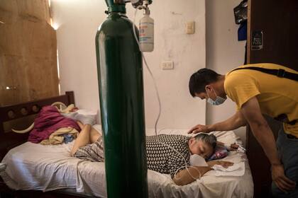 Elena Ruiz, de 53 años, respira oxígeno como parte de su tratamiento de recuperación del COVID-19, mientras su hijo Antony la cuida, en Lima, Perú