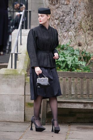 Elle Fanning vistió un conjunto de la firma de la diseñadora: falda midi plisada, chaqueta negra con peplum, cuello alto, hombros pronunciados y sombrero pillbox con velo corto de encaje.