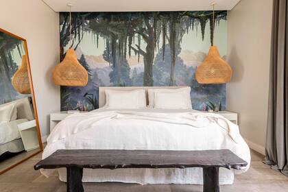 Empapelado (Sofía Willemoes), lámparas (Woodmarket). Respaldo de pana off white, ropa de cama de lino, banqueta de madera quemada, mesas de noche laqueadas en blanco con herraje dorado, espejo con marco de petiribí (todo de Métier Studio).