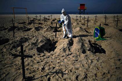 Un activista de la ONG Río de Paz, con un traje protector, cava tumbas en la playa de Copacabana para simbolizar a las víctimas del coronavirus durante una protesta contra la estrategia del gobierno 