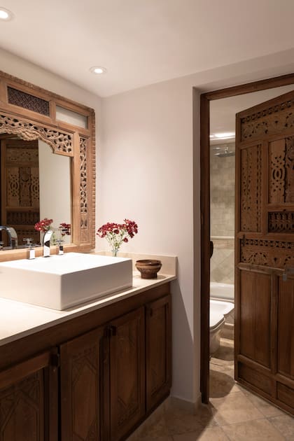 En el baño, puerta de madera tallada a mano (Desde Asia) que, junto al espejo antiguo oriental, se contraponen en estilo a la bacha ‘Tori’ rectangular (Ferrum) con grifería plateada (FV).
