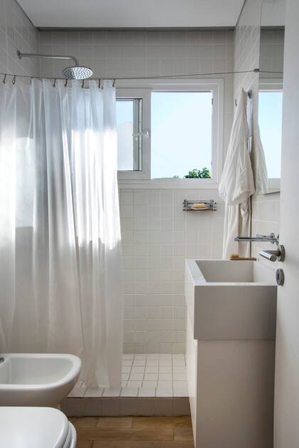 En el baño, revestimiento de cerámicas Pentagres blancas de 5x5. Cortina blanca colgada de un tensor de acero. Vanitory (Mazzinghi-Sánchez Arquitectos) con bacha de apoyo y grifería de pared.
