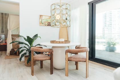 En el comedor de "La orilla", mesa redonda blanca con base oval y sillas "Arco" tapizadas (Woodmarket). Lámpara colgante de estructura circular. Vista al balcón con paisajismo de Joseph Paisajismo.