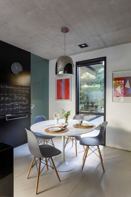 En el comedor diario, mesa ‘Tulip’ blanca y sillas ‘Eames’ grises. Lámpara colgante cromada (Lumishop).