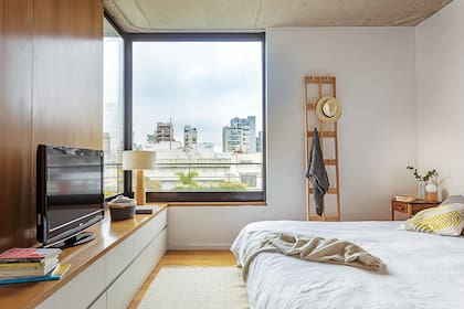 En el cuarto principal, la calidez de la madera está en los pisos, en la pared revestida en incienso y en elementos como la cómoda (diseño de Estudio GMGR), la lámpara (Objetos Luminosos) o el perchero (NET).