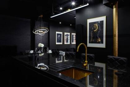En el departamento todo está pintado de negro, como esta cocina, donde lo único que escapa a los tonos oscuros es la canilla y pileta doradas y los marcos de los cuadros