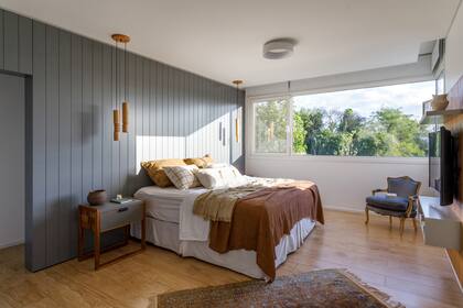 En el dormitorio principal, lámpara de techo y veladores (DIMM). Somier (La Cardeuse) con ropa de cama (Lote Propio). Mesa de luz (Talleres Sustentables) con cuenco de cerámica artesanal (Antes Pella). Sillón heredado y alfombra persa antigua (Decovintage New).