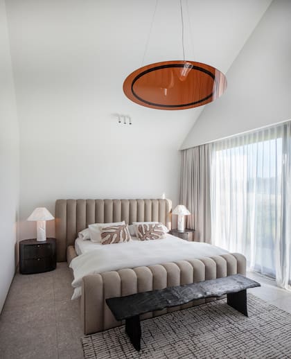 En el dormitorio principal, respaldo (Caro Bianco Interiors), mesas de luz (Hanford) y veladores (Hilaria Luz). Lámpara colgante de acrílico,
diseñada a medida por el Estudio (HDS Ilum). Alfombra (Mihran),
pie de cama (Concepto Calma) y las mismas cortinas (LM Studio) que en el resto de la casa.