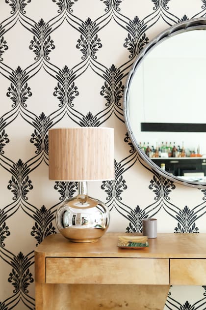 En el hall de entrada, papel con motivos Art Nouveau (Raldua), consola de cuero laqueado (Harturo) y espejo diseñado por la dueña de casa, donde se refleja el comedor