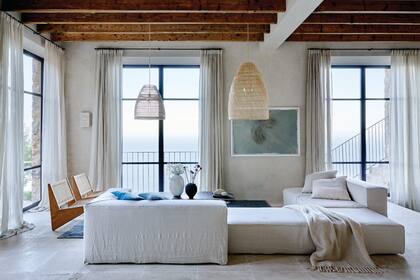 en el living, el sofá modular tapizado en lino, las pantallas de fibras naturales, los almohadones hechos con géneros vintage y las sillas de madera con respaldo de tiento son de More Decor, el brazo de interiorismo del estudio de arquitectura a cargo de esta cuidada reforma. El cuadro es del artista Guillem Nadal. Manta de cashmere (Frette).