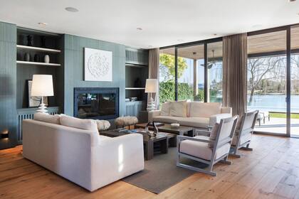 En el living se eligió una paleta neutra en gris azulado y cremas, con chimenea enmarcada en hierro con tachas y vidrio templado. Un modular incluye estantes de laca con estructura de chapa italiana sin lustrar