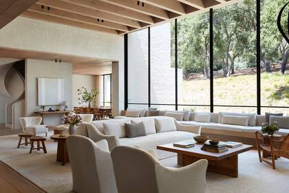 En el living, un sillón con base de madera y fundas en textiles de Larsen y De Le Cuona (Molly Isaksen Interiors) recorre el ventanal. Los butacones vintage son de Gösta Jonsson. Mesas ratonas (Sven Larsson) y alfombras (Mansour).